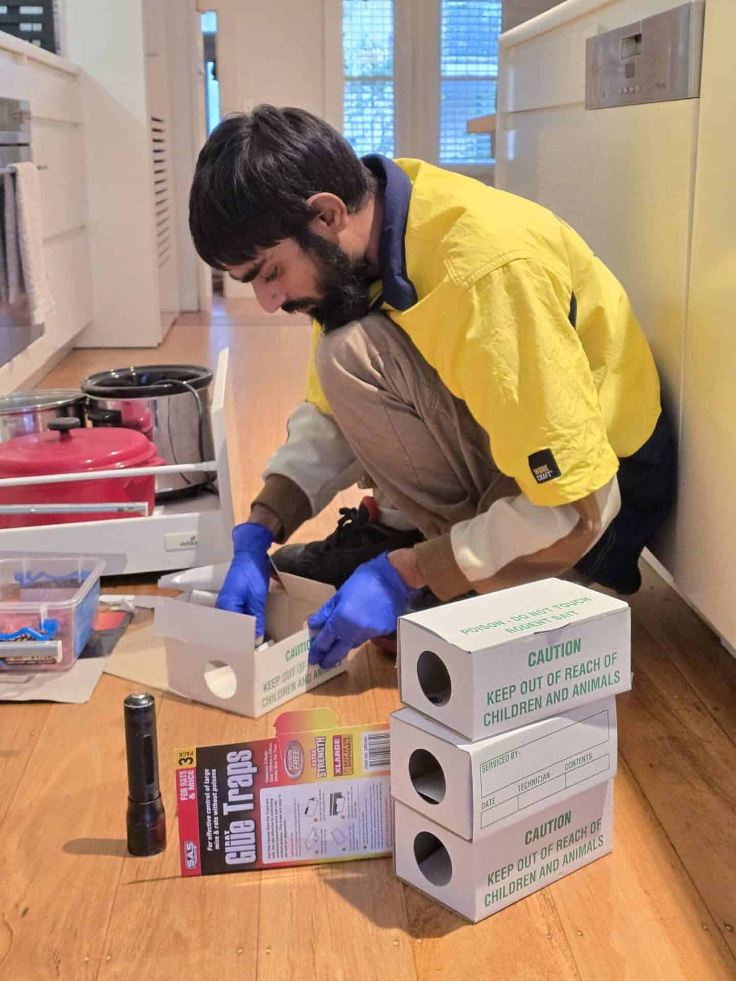 PestOz technician placing a tamper-resistant rodent bait station under a kitchen cabinet in Bondi, Sydney